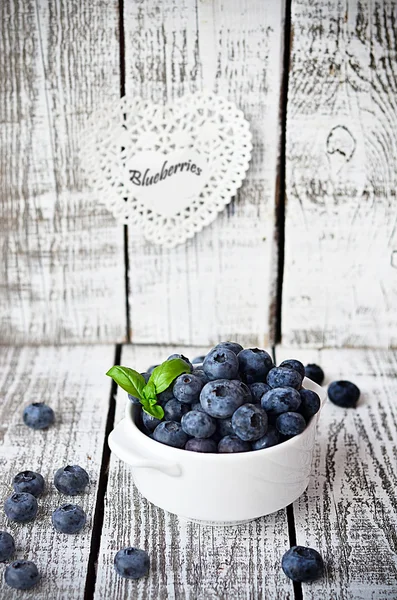 Hvid skål med blåbær på det hvide træbord med basilikumblad - Stock-foto
