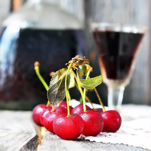 Cherry liquor in the little glasses and big bottle on the vintage napkin on the old wooden background — Stock Photo, Image