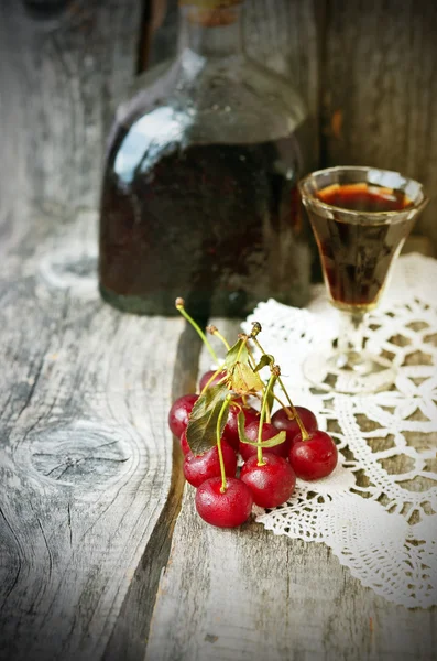 Cherry liquor in the little glasses and big bottle on the vintage napkin on the old wooden background — Stock Photo, Image