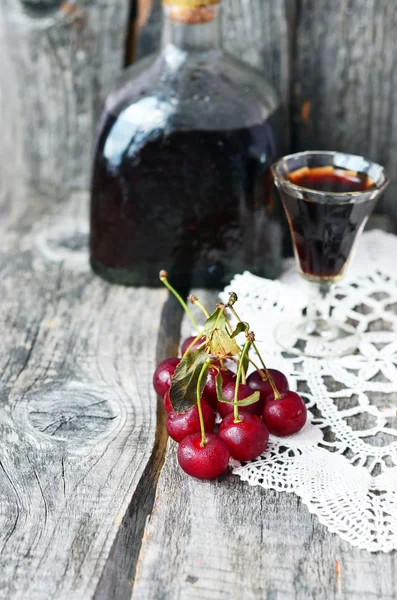 Cherry liquor in the little glasses and big bottle on the vintage napkin on the old wooden background — Stock Photo, Image