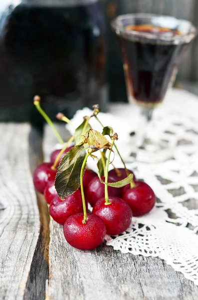 Cherry liquor in the little glasses and big bottle on the vintage napkin on the old wooden background — Stock Photo, Image