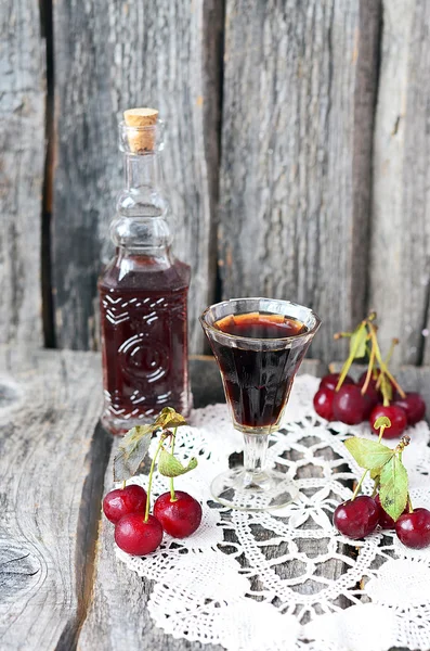 Třešňový likér v malé sklenice a velké vintage na vinobraní ubrousek na staré dřevěné pozadí — Stock fotografie