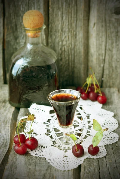 Cherry liquor in the little glasses and big bottle on the vintage napkin on the old wooden background — Stock Photo, Image