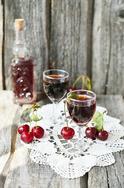 Cherry liquor in the little glasses and big bottle on the vintage napkin on the old wooden background — Stock Photo, Image