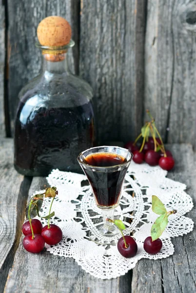 Cherry liquor in the little glasses and big bottle on the vintage napkin on the old wooden background — Stock Photo, Image