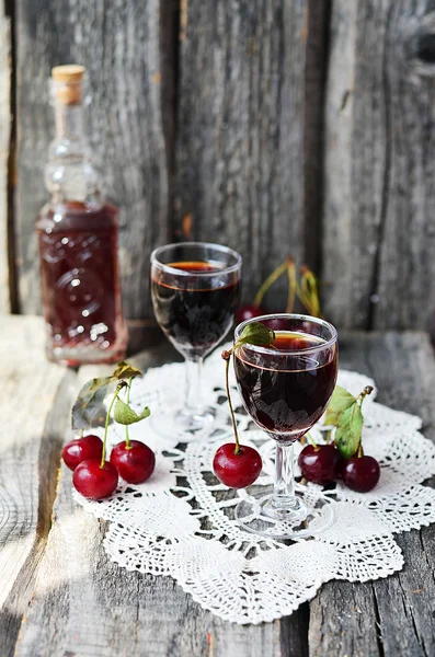 Cherry liquor in the little glasses and big bottle on the vintage napkin on the old wooden background — Stock Photo, Image