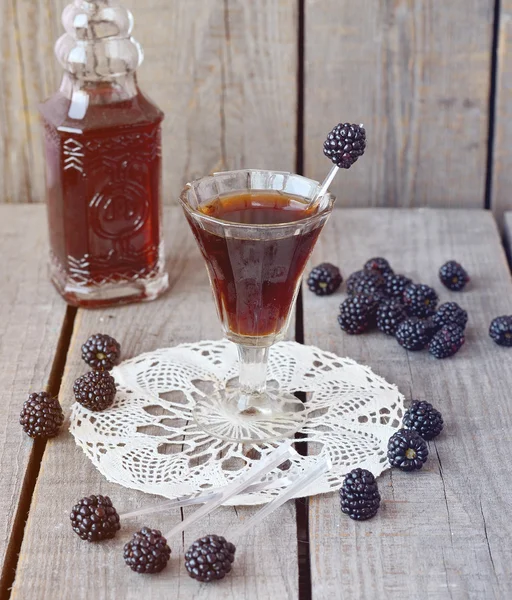 Blackberry liquor in the little glass and vintage bottle on the vintage napkin on the old wooden background, toned picture, selective picture — Stock Photo, Image