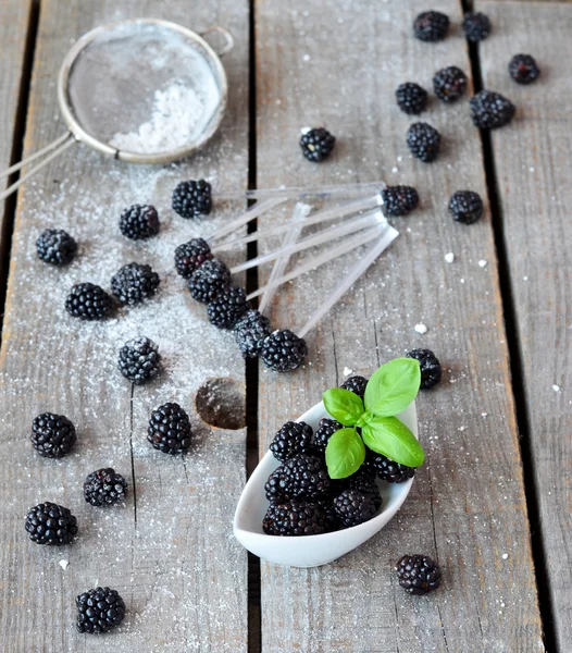 Blackberries in the little white bowl with basil leaf and sugar powder on the old wood background, selective focus — Stock Photo, Image