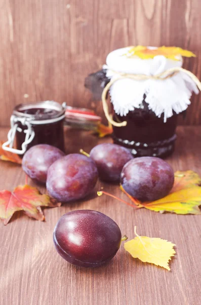 Plum jam and plums with autumn colorful leaves on the wooden background, selective focus, toned focus — Stock Photo, Image