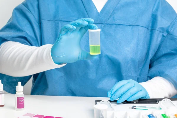 Tıbbi takım elbiseli laboratuvar asistanı ve eldivenleri elinde test edilen suyun bir örneğini tutuyor. Yakın plan, suyun test edilme süreci.