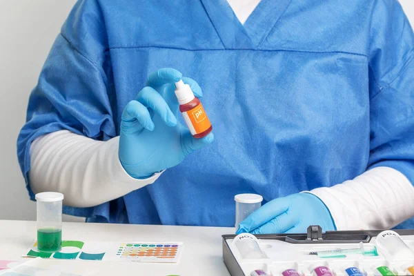 Mavi takım elbiseli ve eldivenli bir laboratuvar asistanı su testi ve akrium bakımı konsepti için Ph reaktifi bulundurur.