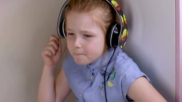 A mało słodkie ruda dziewczyna w niebieski sukienka siedzi w słuchawki, sprawia, że muzyka i śpiewa, tańce — Wideo stockowe