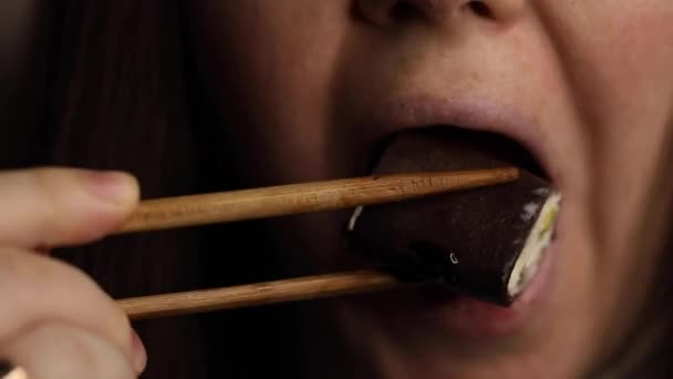Νεαρή γυναίκα με σκούρα μαλλιά τρώει γλυκά ρολά με κινέζικα ξυλάκια κοντά — Αρχείο Βίντεο
