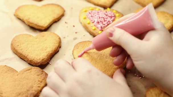 Kadın kalp şeklindeki kurabiyeleri pembe krema, yakın çekim, pişirme süreci ve romantik konseptle süslüyor. — Stok video