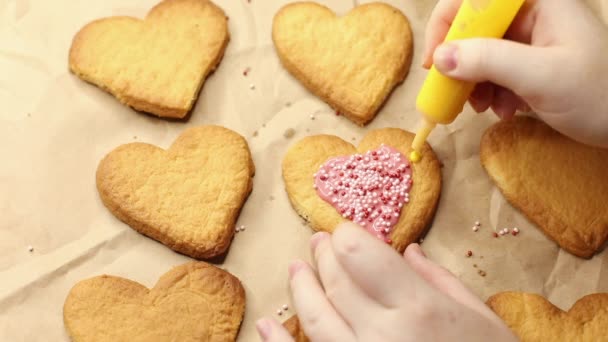 Жінка прикрашає печиво у формі серця жовтим глазур'ю, крупним планом, процес випічки, романтична концепція — стокове відео