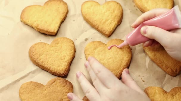 女性はピンクのアイシング、クローズアップ、ベーキングプロセス、ロマンチックなコンセプトでハート型のクッキーを飾ります — ストック動画