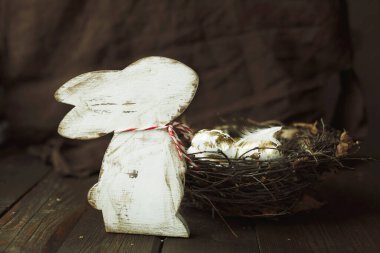 Paskalya arkaplanı, tavşan figürlü ve eski tarz koyu ahşap arka planda bir yuvada altın paskalya yumurtaları.