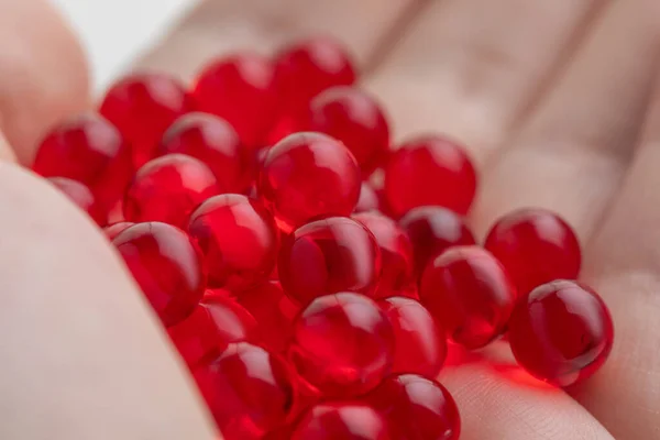 Elinde bir avuç dolusu kırmızı E vitamini kapsülü, yakın plan, tıbbi arka plan.