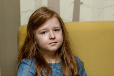 Uzun kızıl saçlı küçük bir kızın portresi oturur ve kameraya bakar.