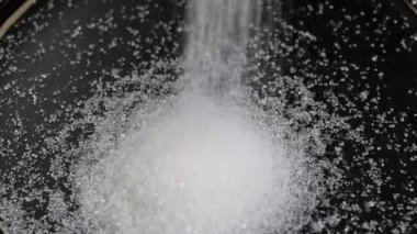 Siyah bir tabağa ya da yakın plan masaya beyaz şeker dökülüyor. Çok şeker, sağlıksız gıda, şeker bağımlılığı, diyabet.