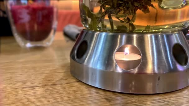 Свеча горит и согревает стеклянный чайник зеленым чаем в уютной атмосфере кафе, копировального пространства, концепции встреч и свиданий — стоковое видео