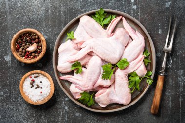 Seramik tabakta taze çiğ tavuk kanatları ve pişirmek için baharatlar.