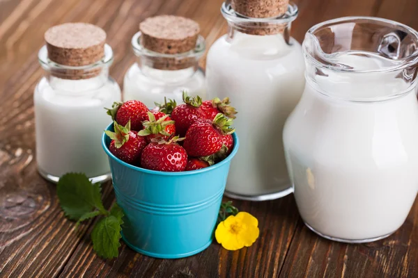 Milk in glass container and a bucket of strawberries