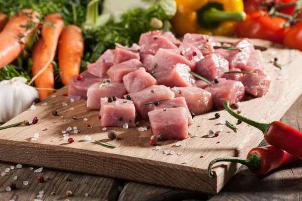 Carne de porco crua sobre tábua de corte e legumes frescos — Fotografia de Stock