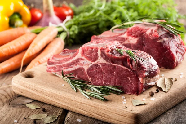 Carne de bovino em bruto sobre tábua de corte e produtos hortícolas frescos — Fotografia de Stock