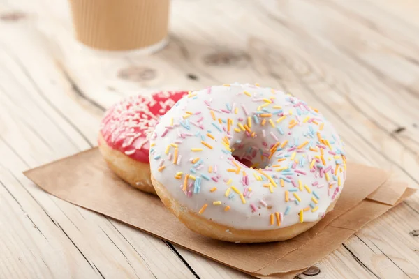Donuts coloridos e xícara de papel na mesa de madeira — Fotografia de Stock