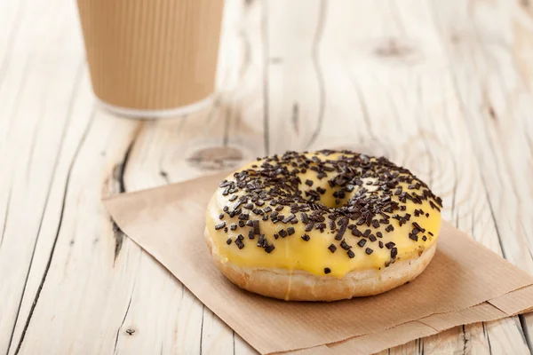 Donut e xícara de papel na mesa de madeira — Fotografia de Stock
