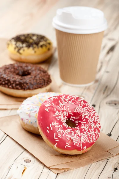 Donuts coloridos e xícara de papel na mesa de madeira — Fotografia de Stock