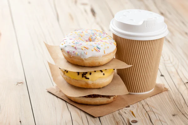 Bunte Donuts und Pappbecher auf Holztisch — Stockfoto