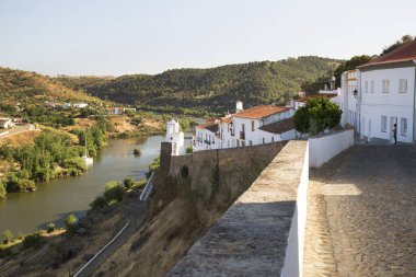 Kırsal nehir manzarası ve binalarda eski çatı kiremitleri ve tepedeki saat kulesinin yanındaki dar caddelerin bulunduğu pitoresk kasaba manzarası.