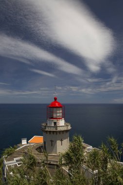 Etrafı doğal bulutlarla çevrili tarihi deniz feneri bir uçurumun tepesine ve limana uzanan dik erişim yoluna ışık hüzmesi veriyor.