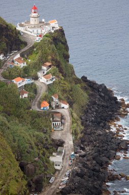 Etrafı doğal bulutlarla çevrili tarihi deniz feneri bir uçurumun tepesine ve limana uzanan dik erişim yoluna ışık hüzmesi veriyor.