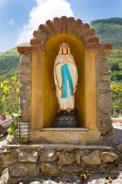 Arka planda yeşil tepeler olan Aziz Maria heykeli