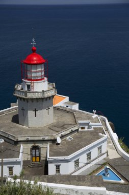 Etrafı doğal bulutlarla çevrili tarihi deniz feneri bir uçurumun tepesine ve limana uzanan dik erişim yoluna ışık hüzmesi veriyor.