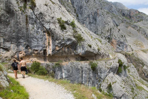 Mountain hikers on a well-known hiking route through a narrow and steep gorge with a carved hiking trail in Northern Spain.