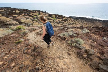 Deniz kenarındaki kayalık bir yolda yürüyen turistlerin görüntüsü