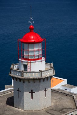 Etrafı doğal bulutlarla çevrili tarihi deniz feneri bir uçurumun tepesine ve limana uzanan dik erişim yoluna ışık hüzmesi veriyor.