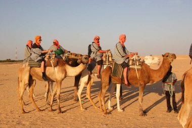 Çölde develerin üzerinde gezen insanların manzarası.