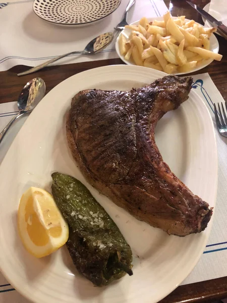 Beyaz tabakta kızarmış patatesli domuz rostosu.