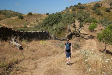 Sırt çantalı bir adam dağlarda yol boyunca yürüyor.