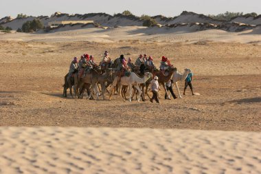Çölde develerin üzerinde gezen insanların manzarası.