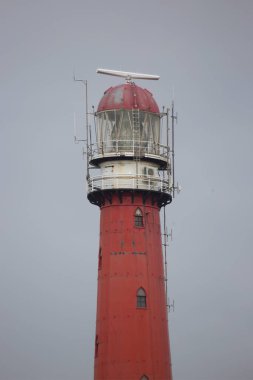 Kum tepeleri yakınlarındaki tarihi yüksek kırmızı deniz feneri ve Hollanda 'nın tipik bir sahil köyündeki hendeğin arkasında güvendeler.