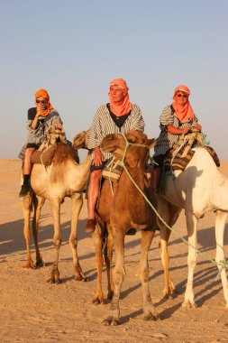 Çölde develerin üzerinde gezen insanların manzarası.