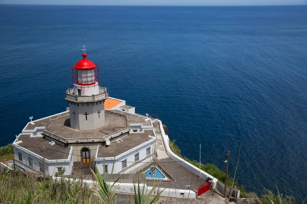 Etrafı doğal bulutlarla çevrili tarihi deniz feneri bir uçurumun tepesine ve limana uzanan dik erişim yoluna ışık hüzmesi veriyor.