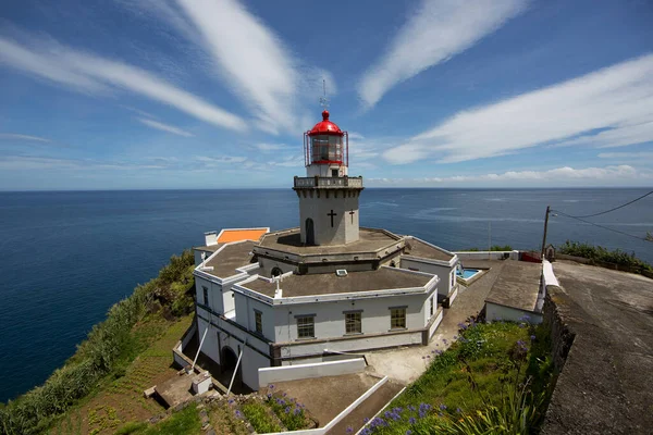 Etrafı doğal bulutlarla çevrili tarihi deniz feneri bir uçurumun tepesine ve limana uzanan dik erişim yoluna ışık hüzmesi veriyor.