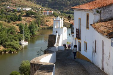 Kırsal nehir manzarası ve binalarda eski çatı kiremitleri ve tepedeki saat kulesinin yanındaki dar caddelerin bulunduğu pitoresk kasaba manzarası.